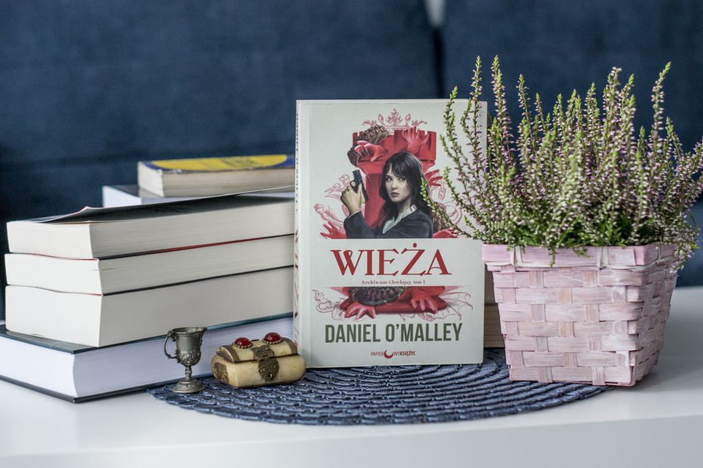 Wieża Daniella O-Malley - książka stoi na placie, po prawej wrzos w koszyku, po lewej stosik innych książek - recenzja książki urban fantasy