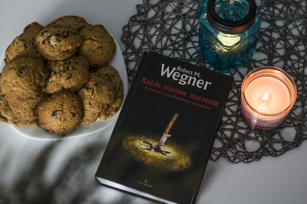 Każde martwe marzenie Robert M. Wegner - książka lezy na blacie w otoczeniu ciasreczkek na talerzu oraz świeczek - recenzja książki high fantasy