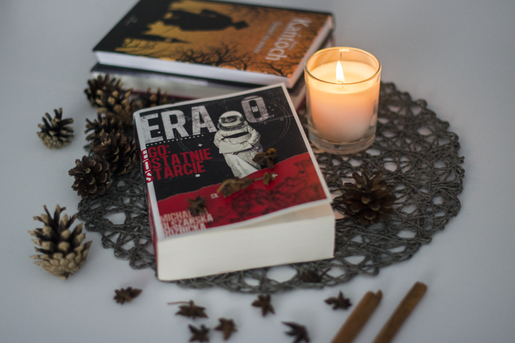 Era Zero. Ego: Ostatnie starcie Michaliny Olszańskiej-Rozbickiej - książka leży na blacie w otoczeniu świeczki, szyszek, lasek cynamonu i książek - ilustracja do recenzji młodzieżowej powieści SF