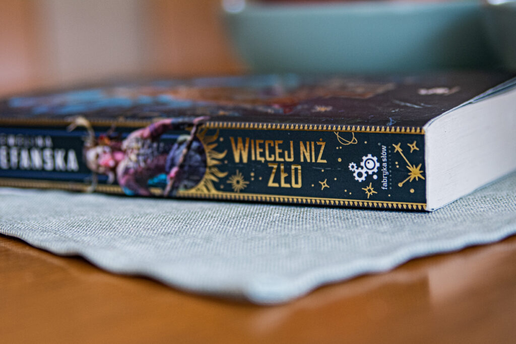 Więcej niż zło Eweliny Stefańskiej - grzbiet książki leży na blacie - ilustracja do recenzji