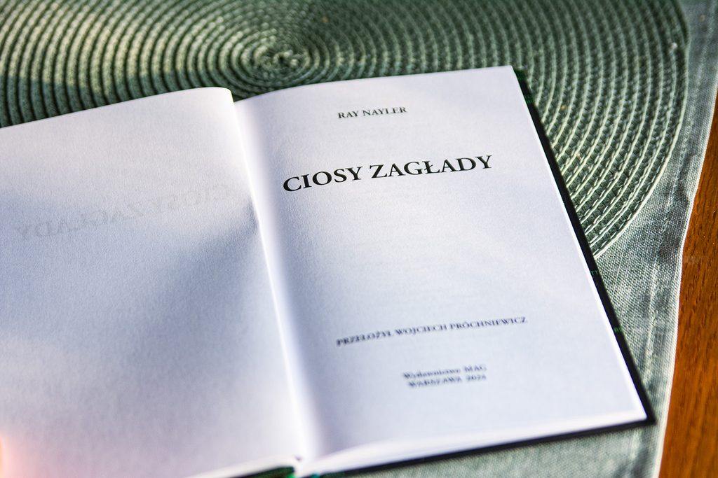 Ciosy zagłady leżą otwarte na blacie; widać stronę tytułową i białe kartki