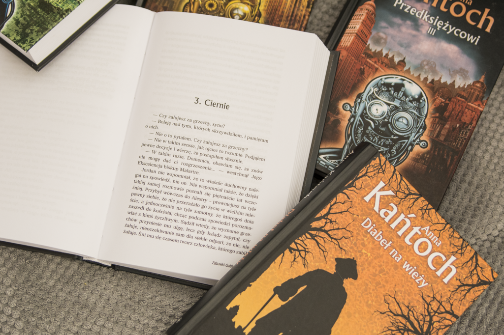 Zabawki diabła Anny Kańtoch - otwarta książka leży na kanapie obok innych książek Anny Kańtoch - ilustracja do recenzji historycznego fantasy