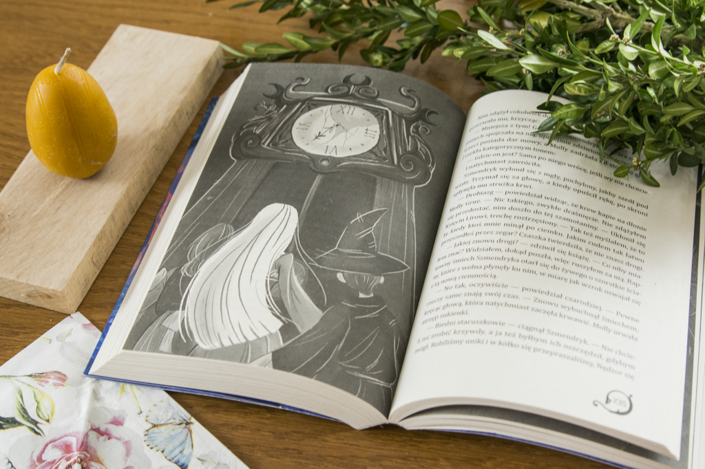 Ostatni jednorożec Petera S. Beagle - otwarta książa fantasy leży na stole. Ilustracja na kartce przedstawia wielki zegar a przed nim trzy postacie