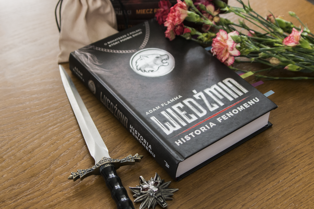 Wiedźmin. Historia fenomenu Adama Flammy - książka leży na blacie wśród ozdób