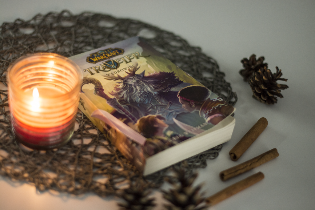 World of Warcraft. Traveller. Wędrowiec Greg Weisman - książka na blacie w otoczeniu świeczki, szyszek i lasek cynamonu - ilustracja do recenzji książki fantasy dla młodzieży