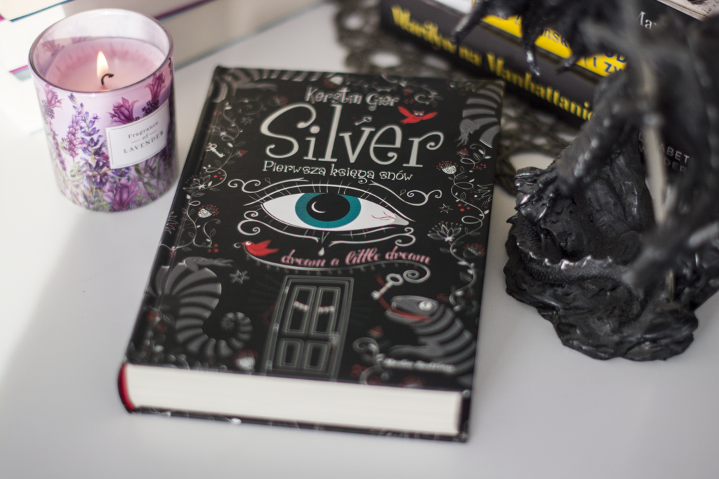 Silver Kerstin Gier - książka leży na blacie w otoczeniu książek, świeczki i fiugrki smoka - ilustracja do recenzji powieści fantasy dla młodzieży