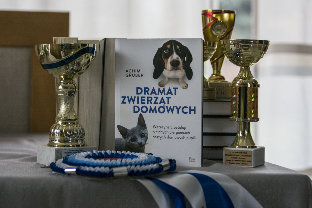 Dramat zwierząt domowych - książka stoi na stole w otoczeniu pucharów i rozet - ilustracja do recenzji książki